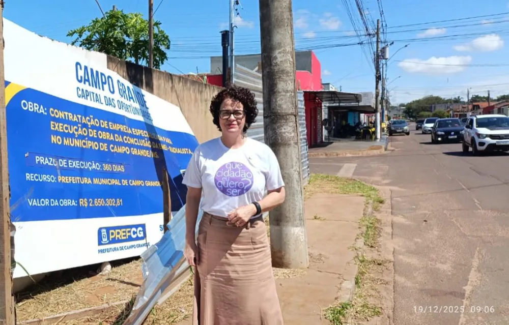 Voluntária da Força-Tarefa Cidadã em frente à placa de uma obra de educação infantil em Campo Grande (MS)